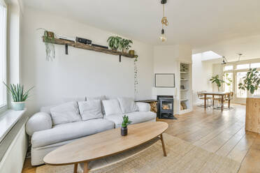 Bequemes Sofa mit Kissen und kleiner runder Couchtisch in einem geräumigen hellen Wohnzimmer mit weichem Teppich auf Holzboden und weißen Wänden in der Nähe des Kamins - ADSF41550