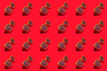 Muster von Reihen von Sonnenbrillen im Retro-Stil flach auf rotem Hintergrund gelegt - GIOF15699