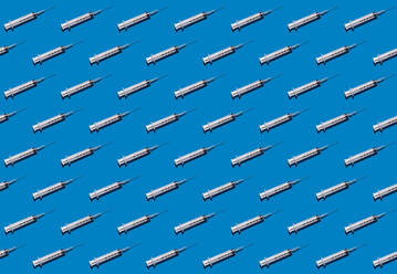 Muster von Reihen von Spritzen flach vor blauem Hintergrund gelegt - GIOF15700