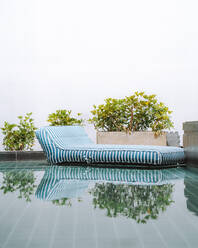 Striped inflatable lounger on calm mirror surface of pool in resort area with green plants - ADSF41580