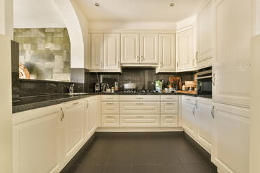 Theke mit weißen Schränken und modernen Einbaugeräten in heller, stilvoller Küche mit Gasherd in geräumiger Wohnung - ADSF41655