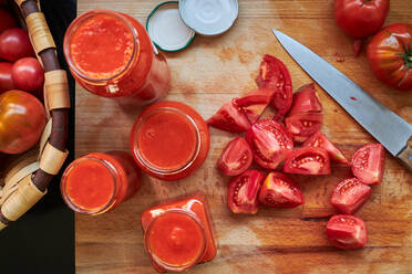 Top view of ripe red tomatoes and jars of sauce placed on table in kitchen - ADSF41690