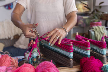 Crop lady with scissors cutting multicolored yarn on loom during work in blurred creative studio - ADSF41718