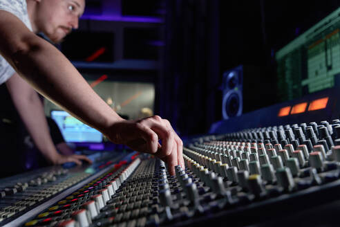 Männlicher Tontechniker mit Mischpult bei der Bearbeitung von Geräuschen im Studio während der Aufnahme eines Songs - ADSF41737