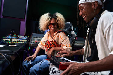 Positiv geschnittener afroamerikanischer Mann spielt Musik auf einem Synthesizer, während er mit einer Frau in einem modernen Aufnahmestudio probt - ADSF41751