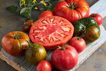 Hohe Winkel der geschnittenen Tomate mit Salz auf hölzernen Schneidebrett zwischen reifen roten Tomaten mit Wassertropfen platziert - ADSF41926