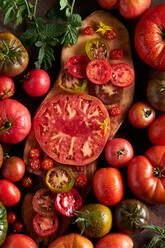 Hohe Winkel der geschnittenen Tomate mit Salz auf hölzernen Schneidebrett zwischen reifen roten Tomaten mit Wassertropfen platziert - ADSF41930