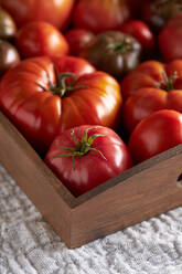 Draufsicht auf frische reife rote Tomaten in einer Holzkiste auf einer Leinenserviette auf dem Tisch - ADSF41936