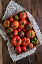 Top view of fresh ripe red tomatoes in wooden box placed on linen napkin on table - ADSF41937