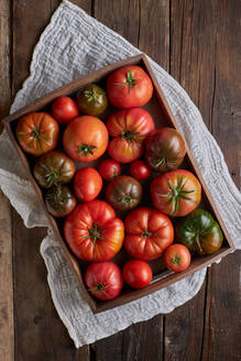 Draufsicht auf frische reife rote Tomaten in einer Holzkiste auf einer Leinenserviette auf dem Tisch - ADSF41937