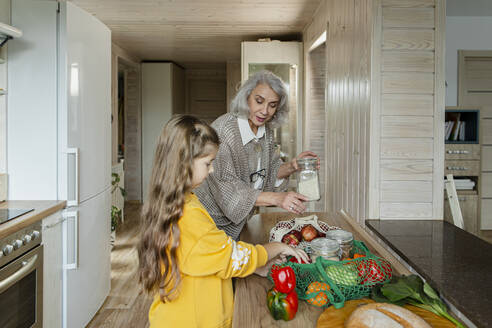 Grandmother and granddaughter unpacking fresh groceries in kitchen - LLUF00966