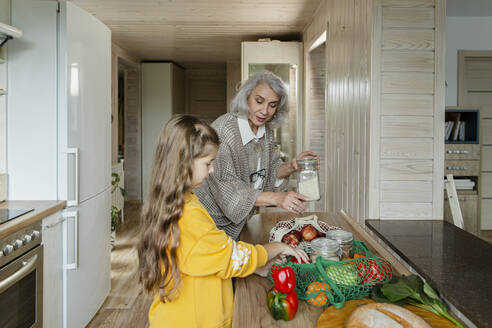 Großmutter und Enkelin packen in der Küche frische Lebensmittel aus - LLUF00966