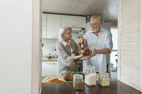 Senior couple holding fresh apples in kitchen - LLUF00967