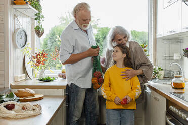 Grandparents and granddaughter unpacking fresh groceries in kitchen - LLUF00973