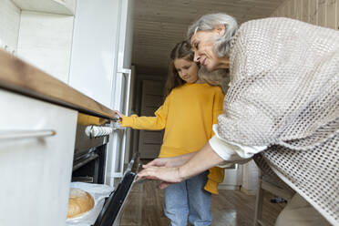 Großmutter und Enkelin nehmen frisch gebackenes Brot aus dem Ofen - LLUF00980