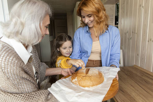 Großmutter, Mutter und Enkelin mit frisch gebackenem Brot in der Küche - LLUF00981