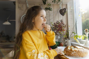 Mädchen probiert frisch gebackenes Brot in der Küche - LLUF00982