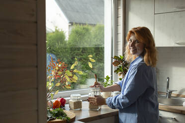 Lächelnde Frau in der Küche am Fenster stehend - LLUF00987