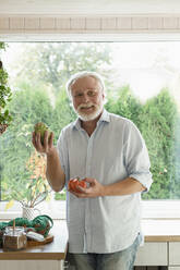 Porträt eines reifen Mannes mit frischem Gemüse in der Küche - LLUF00992