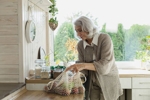 Senior woman unpacking fresh groceries in kitchen - LLUF00993