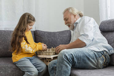 Grandfather and granddaughter bunching waste paper together on sofa - LLUF01000