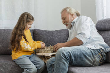 Großvater und Enkelin bündeln Altpapier auf dem Sofa - LLUF01000