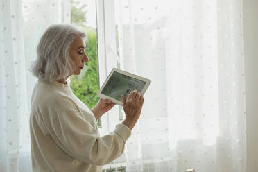 Senior woman adjusting temperature on smart home device - LLUF01005