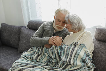 Älteres Paar kuschelt auf der Couch unter einer Decke - LLUF01010