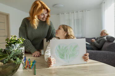 Mädchen mit Mutter am Tisch, die eine Zeichnung zeigt - LLUF01018