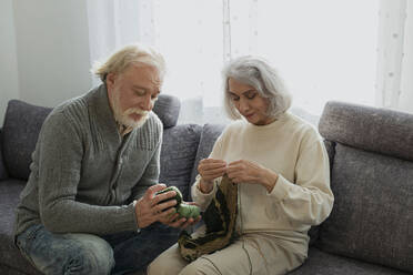 Senior couple sitting on couch knitting - LLUF01019