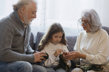 Grandparents teaching crocheting to granddaughter on couch - LLUF01020