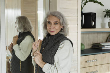 Porträt einer selbstbewussten älteren Frau vor einem Spiegel zu Hause - LLUF01027