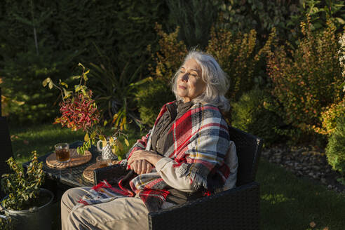 Ältere Frau sitzt im Herbst in einem Sessel im Garten - LLUF01032