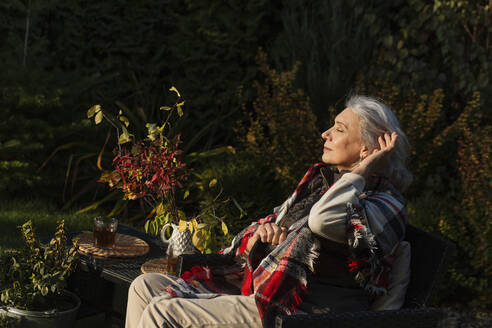 Ältere Frau sitzt im Herbst in einem Sessel im Garten - LLUF01033