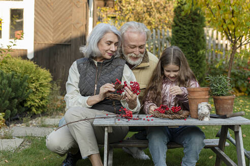 Großeltern und Enkelin sitzen am Gartentisch und basteln mit Eberesche - LLUF01035