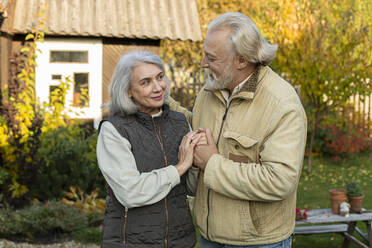 Zärtliches älteres Paar hält sich im Garten an den Händen - LLUF01037