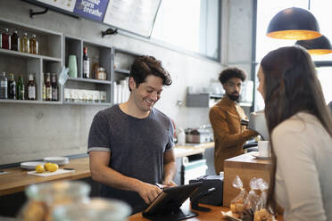 Lächelnder Barista mit Tablet-PC am Tresen eines Cafés - NURF00009