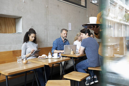 Kunden, die drahtlose Geräte benutzen, sitzen am Tisch in einem Café - NURF00013