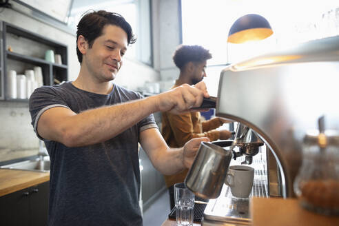 Lächelnder Barista mit dampfender Milch im Café - NURF00014