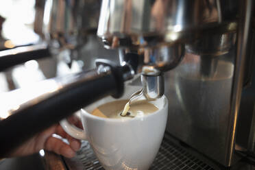 Die Hand eines Barista hält eine Tasse unter einer Espressomaschine, die Milch ausgießt - NURF00018