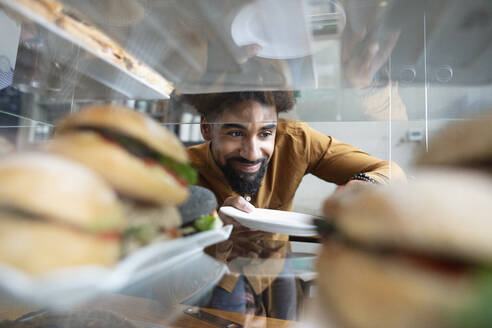 Smiling cafe owner removing burger from display cabinet at coffee shop - NURF00019