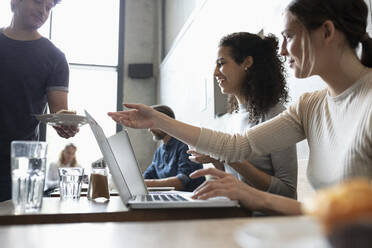 Businesswoman with laptop taking food from waiter in cafe - NURF00023