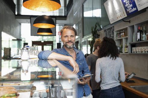 Lächelnder Café-Besitzer mit Tablet-PC im Café stehend - NURF00029