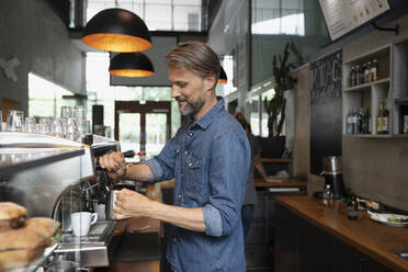 Lächelnder Barista mit dampfender Milch im Café - NURF00044