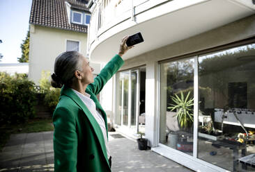 Senior businesswoman photographing house through smart phone - FLLF00819