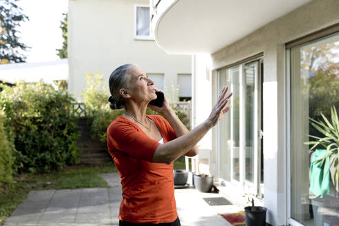 Ältere Frau, die vor einem Haus mit einem Mobiltelefon spricht - FLLF00825