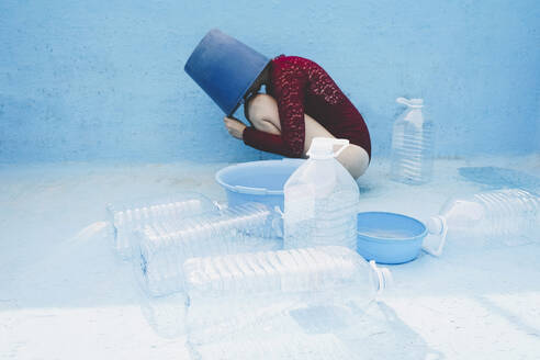 Woman with head inside bucket by plastic bottles in empty swimming pool - SVCF00229