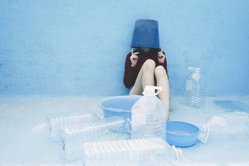 Woman wearing swimwear sitting with head inside bucket by plastic bottles - SVCF00230