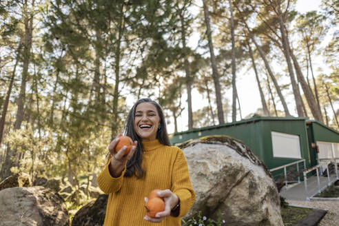 Ältere Frau steht im Garten und jongliert mit Bio-Orangen - JCCMF08423