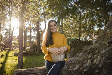 Smiling mature woman holding a wicker basket in nature - JCCMF08471